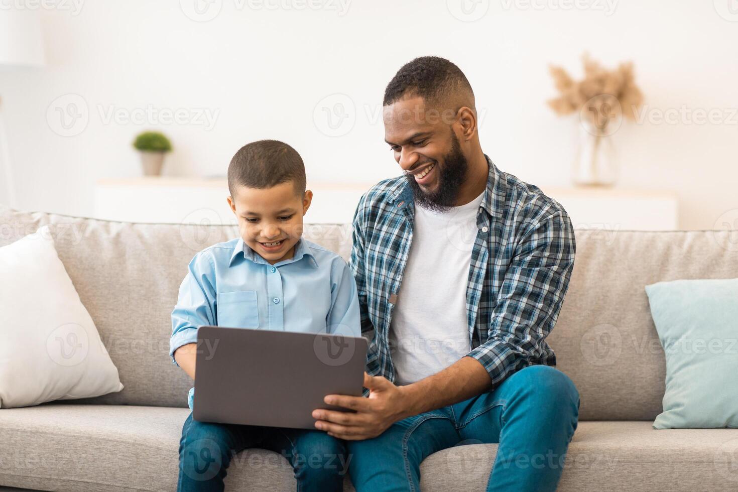 African American Father Teaching Son To Use Laptop Browsing Internet At Home. Little Boy And His Dad Browsing Internet Or Watching Movie Online Together On Weekend. Modern Gadgets Lifestyle photo
