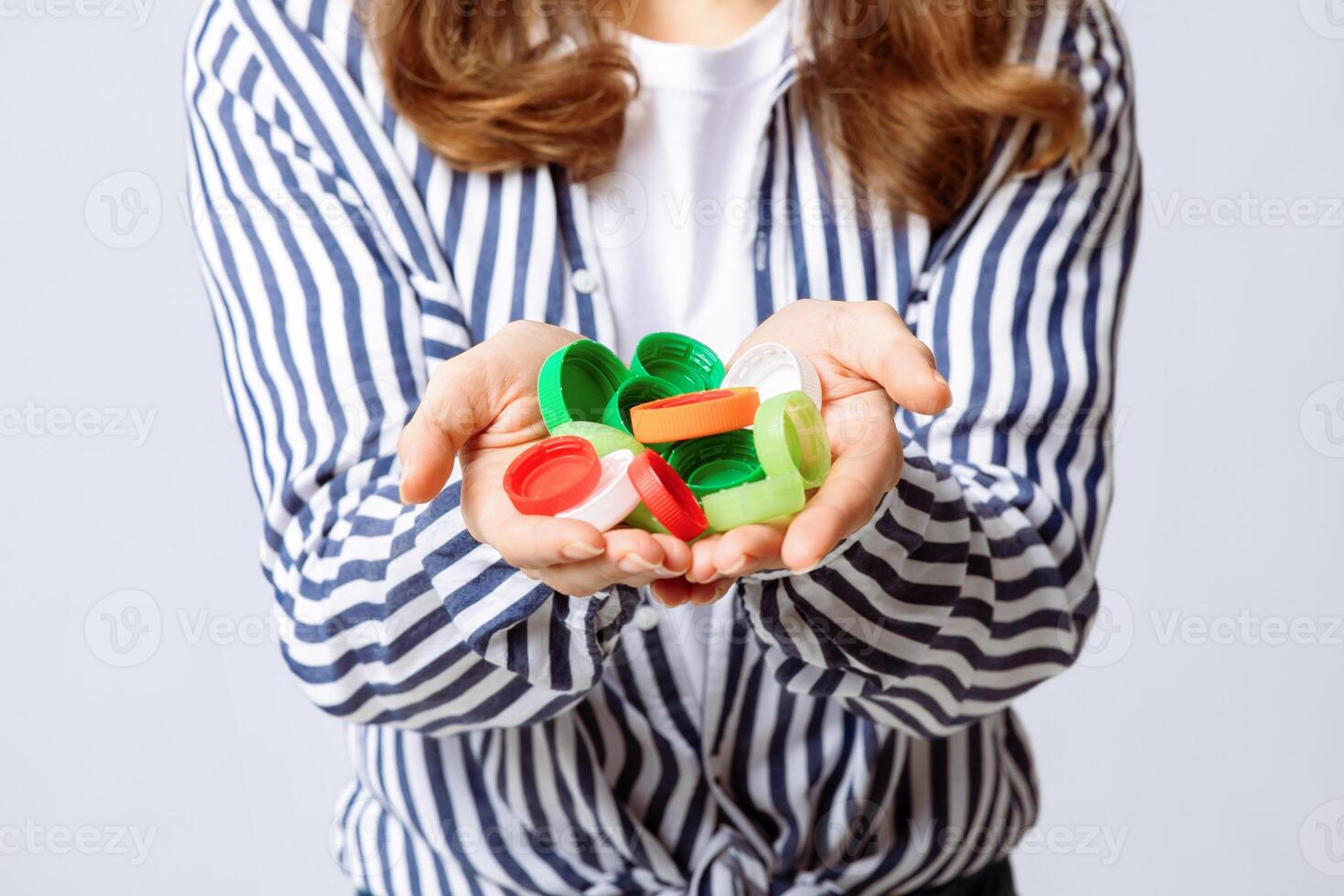 A woman is actively engaging in recycling by holding a collection of colorful plastic bottle caps in her hands. Her eco-friendly approach reflects awareness for environmental sustainability. photo