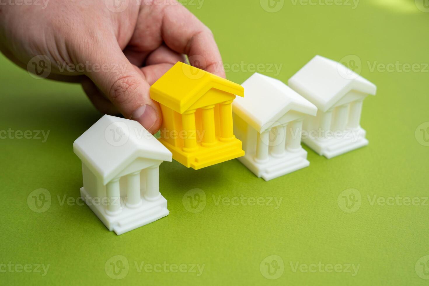 Hand choosing yellow bank building. Choosing the best banking for business and investment. Services, trust, capital strategy. Creditworthiness, economic decisions. photo