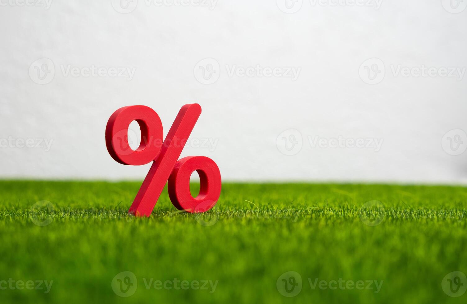 A red percentage sign stands on the grass. Deposits and finances. Interest rates on agricultural loans, taxes on land, or environmental levies. Rural development bonds photo