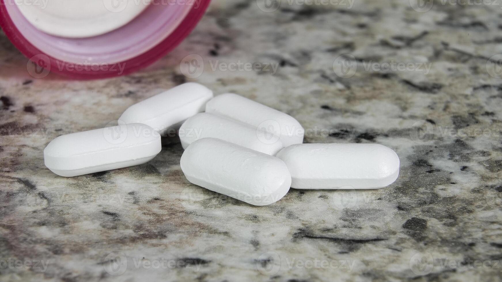 Tablets spilled from a prescription bottle onto a granite countertop photo
