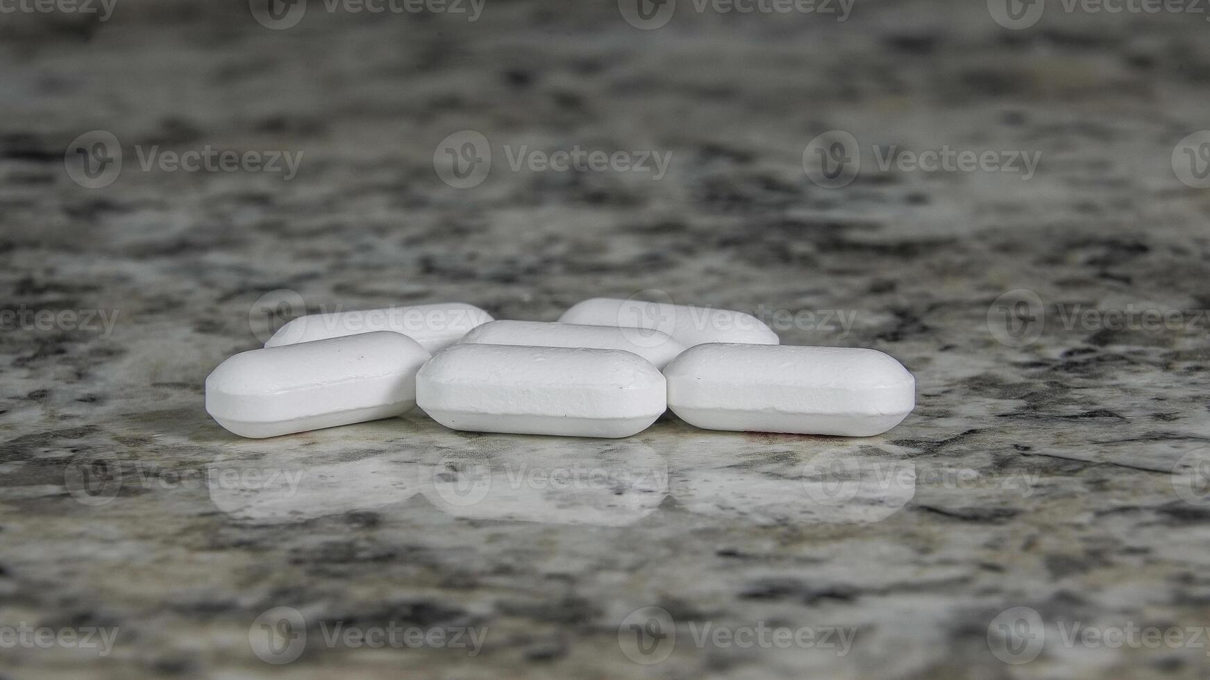 Six white pills are scattered on a light colored stone countertop photo