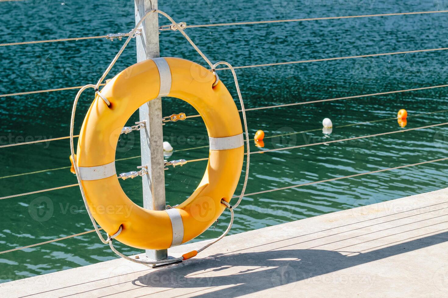 Lifebuoy tied to railing near calm water with floating buoys on a sunny day photo