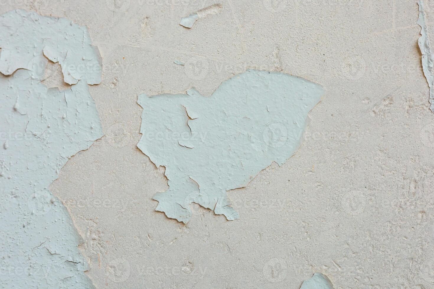 Cracked and peeling paint on a textured wall in a sunlit room revealing layers beneath photo