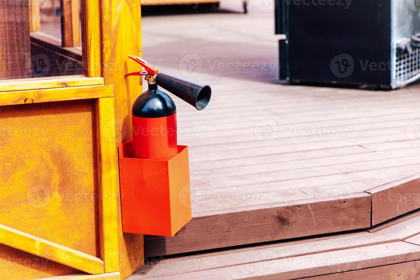 Fire extinguisher mounted on wooden structure near outdoor seating area photo