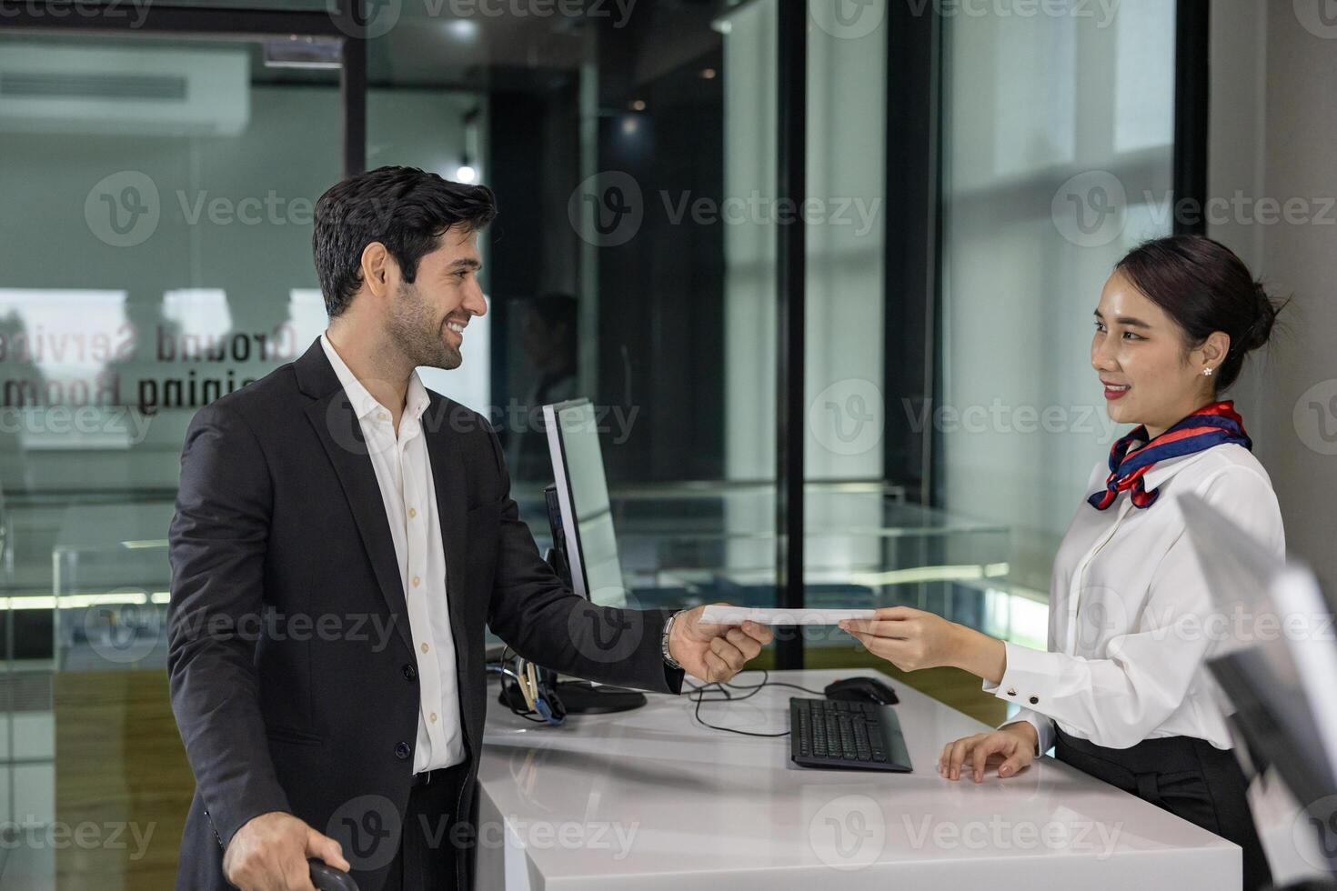 Caucasian businessman passenger is receiving boarding pass from the airline ground crew at check in counter at departure terminal into the airplane for final inspection before boarding the plane photo