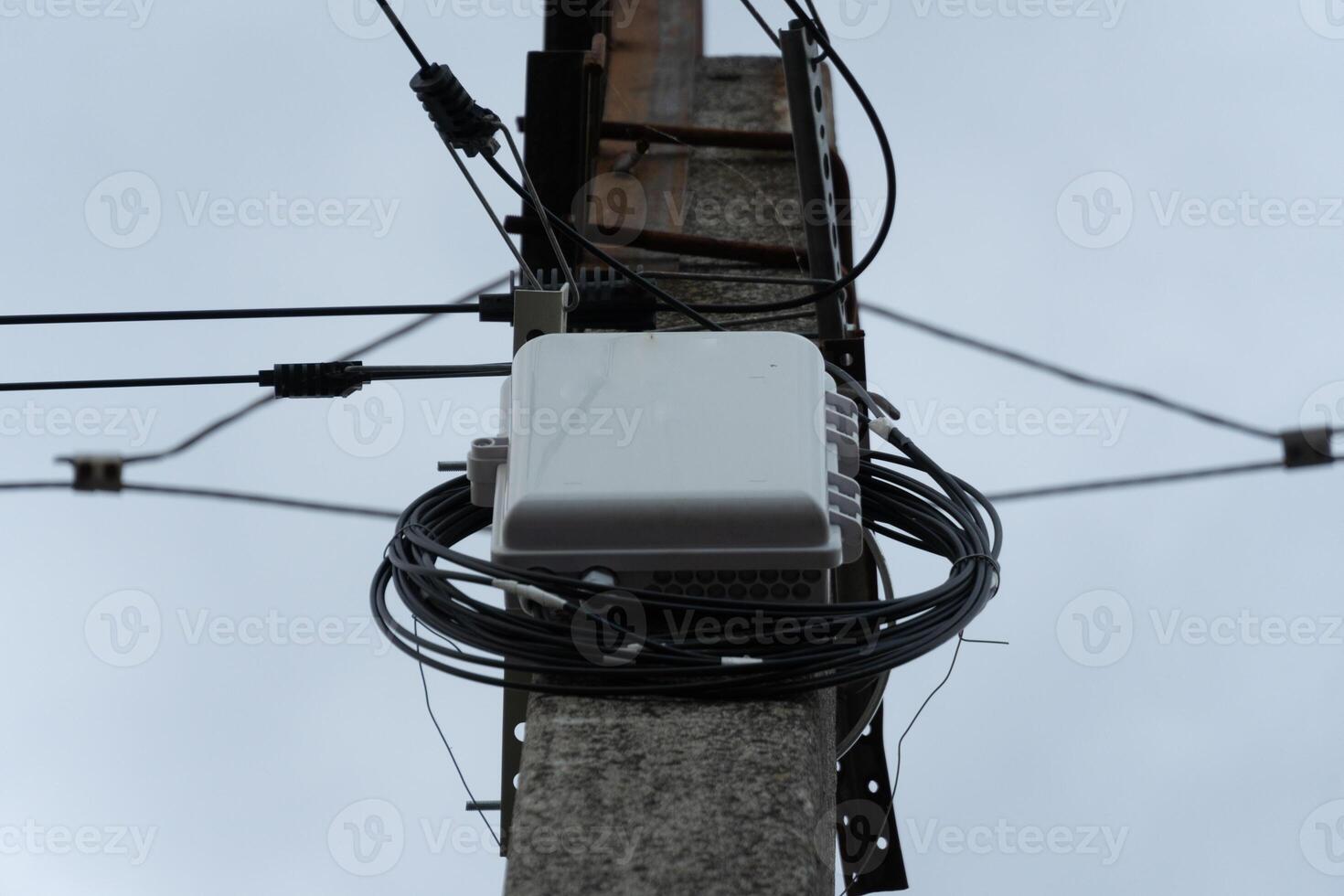 Communication equipment attached to a utility pole, surrounded by tangled wires, set against a backdrop of a grey overcast sky with minimal visibility photo