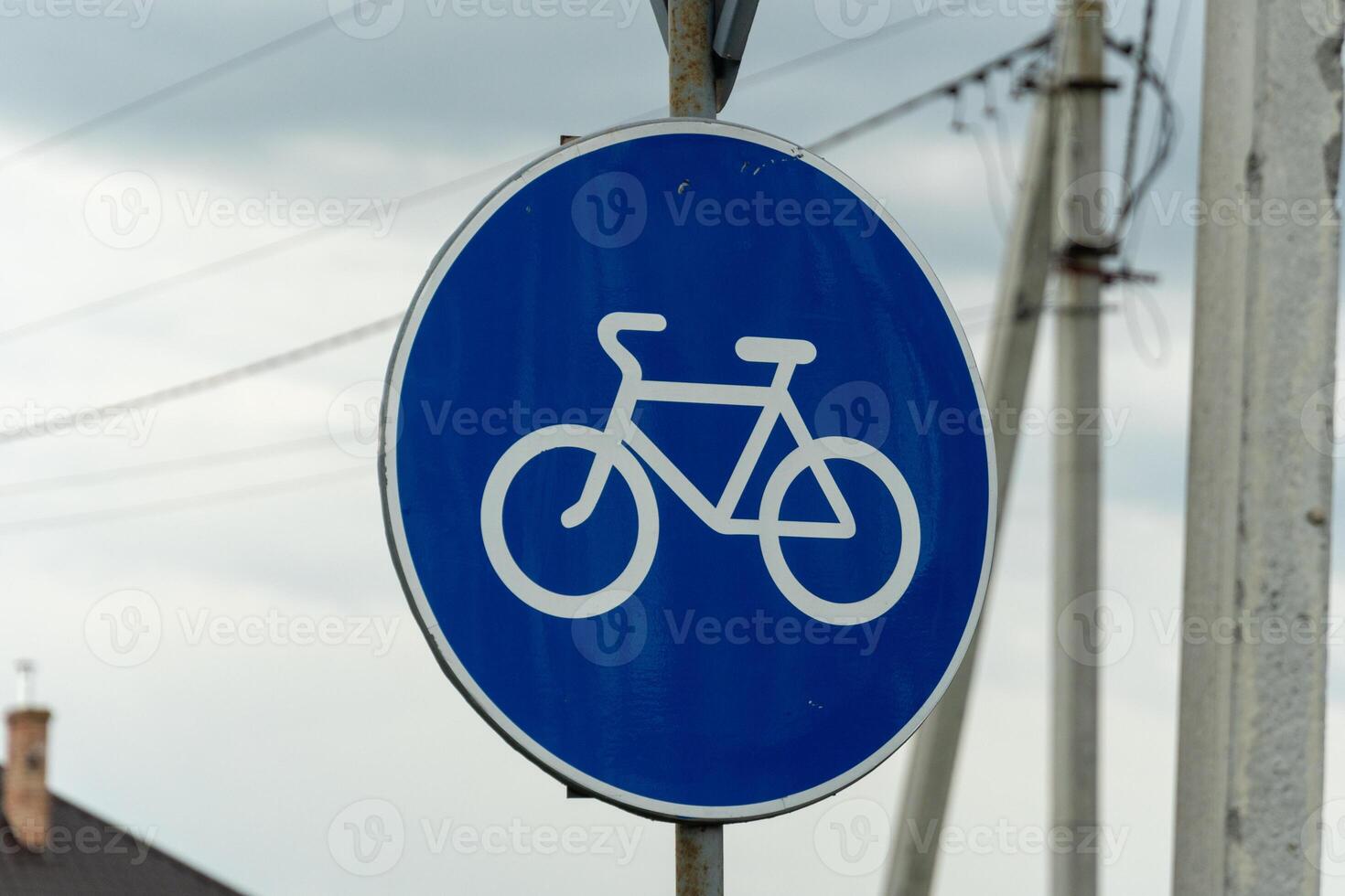 A blue circular sign displays a white bicycle icon, marking a designated lane for cyclists in an urban setting under overcast skies photo