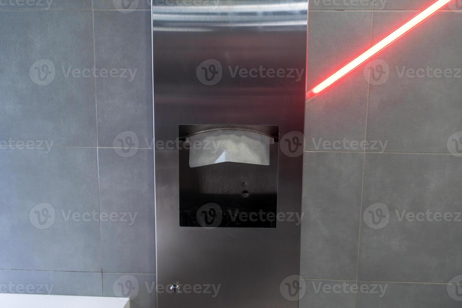 A metallic sanitary disposal unit is mounted on a wall with a red laser indicator, highlighting its functionality in a sleek, modern restroom setting photo