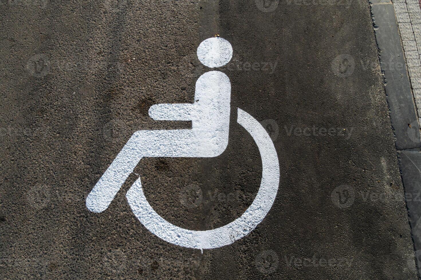 A white accessibility symbol is painted on a gray concrete surface, designating a parking space for individuals with disabilities in an urban setting photo