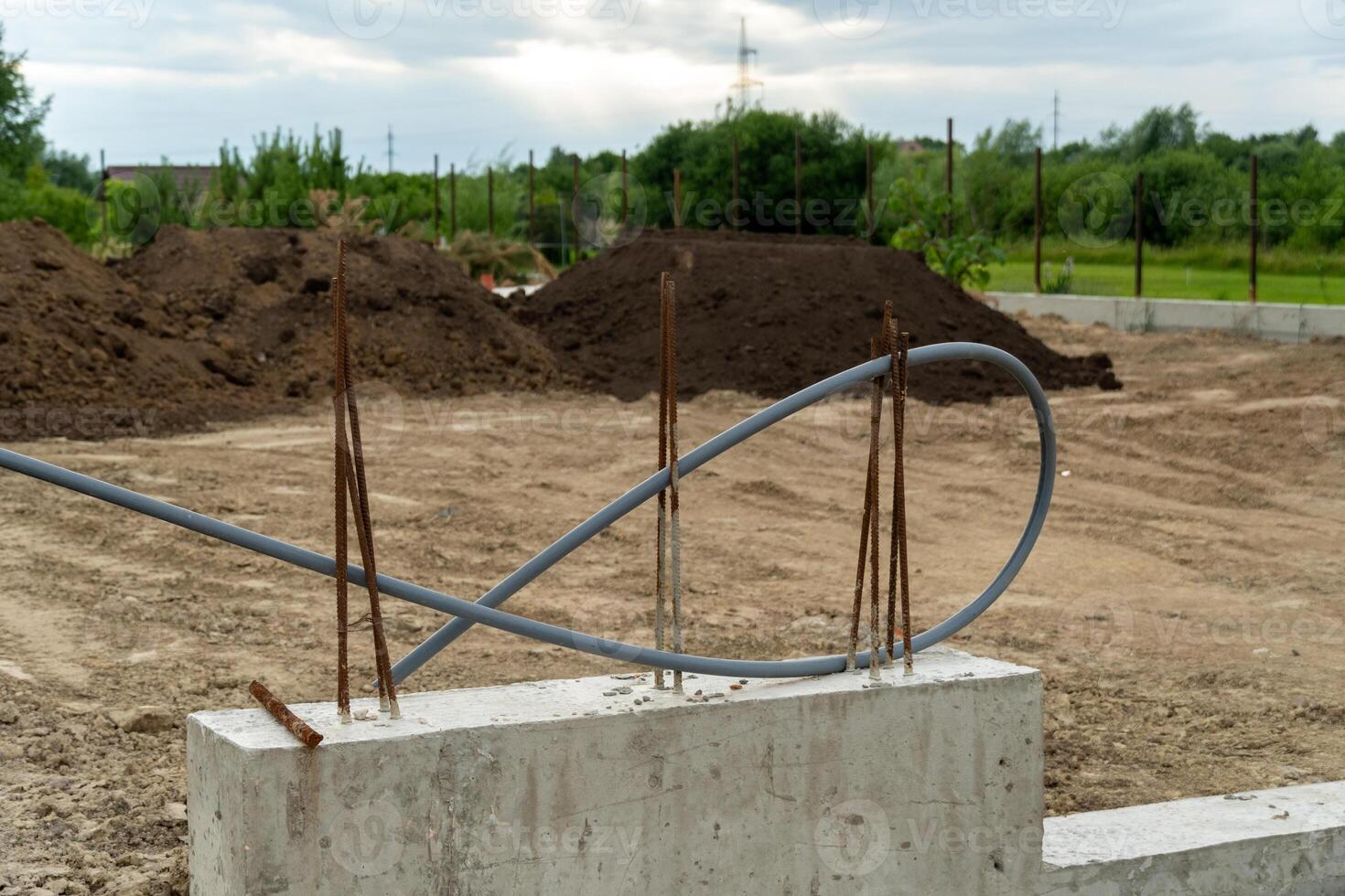 Workers are laying the foundation at a construction site, where rebar and electrical conduit are visible against a backdrop of earth mounds and cloudy skies photo