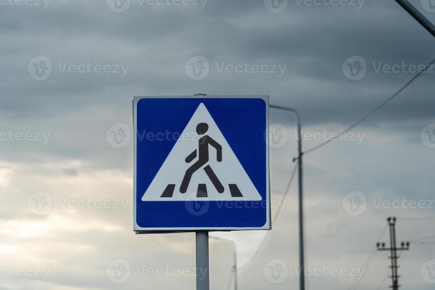 A triangular warning sign alerts pedestrians of construction ahead on a rural road against a backdrop of grey clouds and utility poles photo