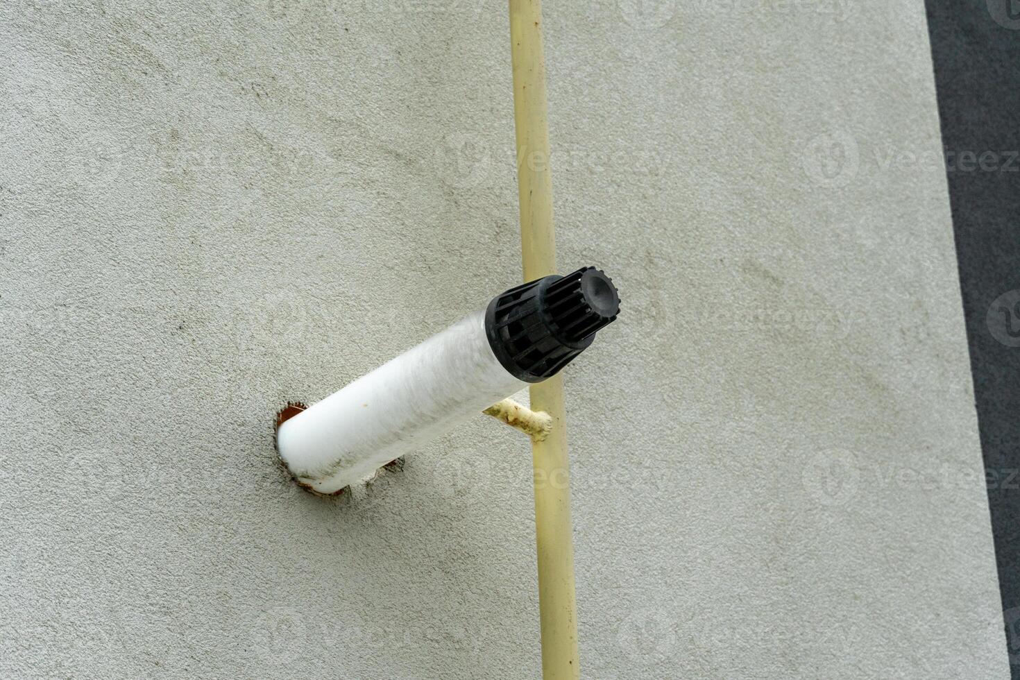 A distinctive air vent extends from a textured wall, showcasing its cylindrical shape and dark cap against a backdrop of cloudy skies and gray surfaces photo