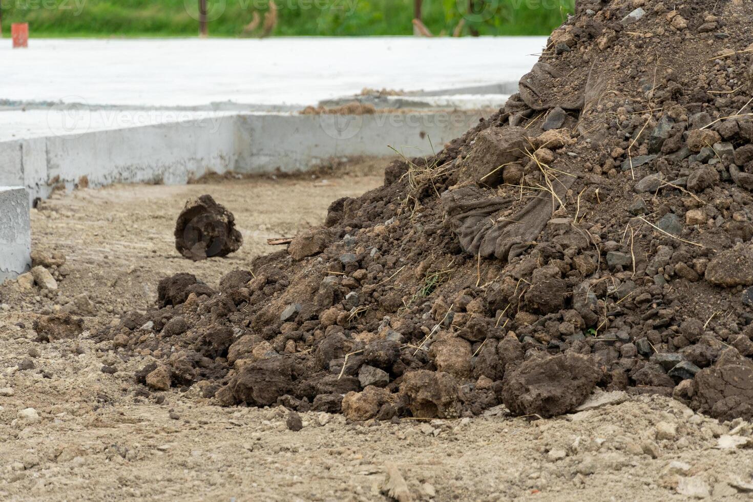 Pile of soil and stones at a construction site, with scattered debris and an unfinished concrete slab visible in the background on a cloudy day photo