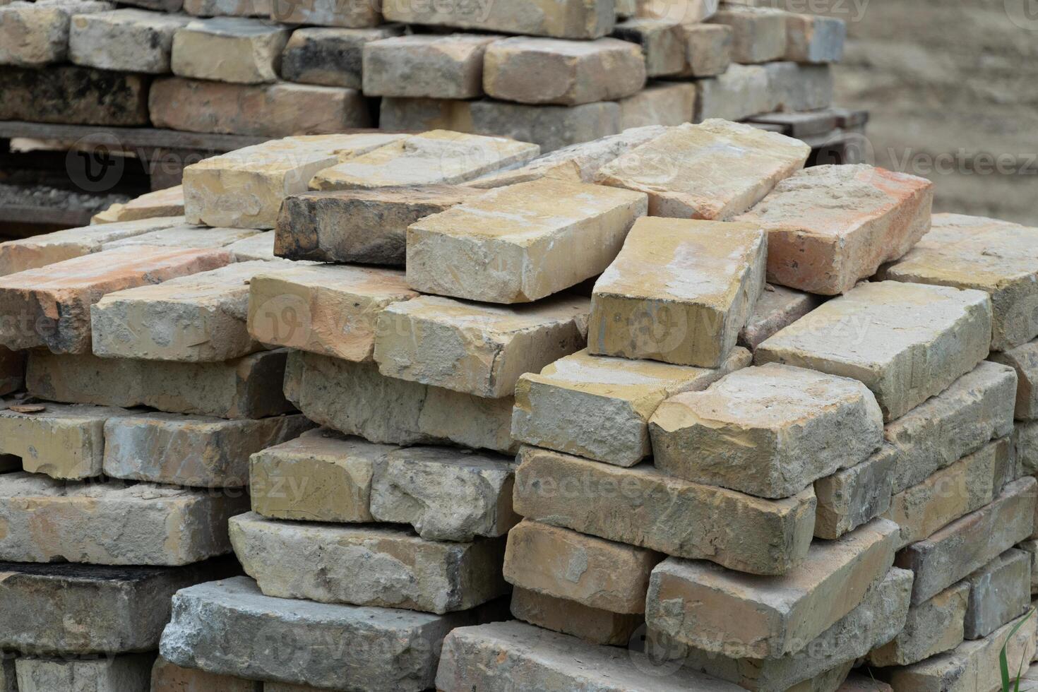 Piles of weathered bricks are arranged neatly at a construction site, waiting to be used in various building projects under clear daylight photo