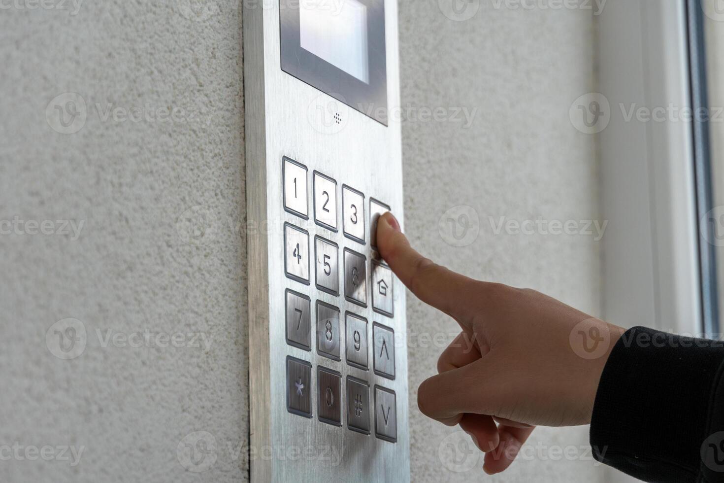 A hand is pressing the number three on a sleek keypad mounted on a wall, likely to gain access to the building, with soft natural light illuminating the area photo