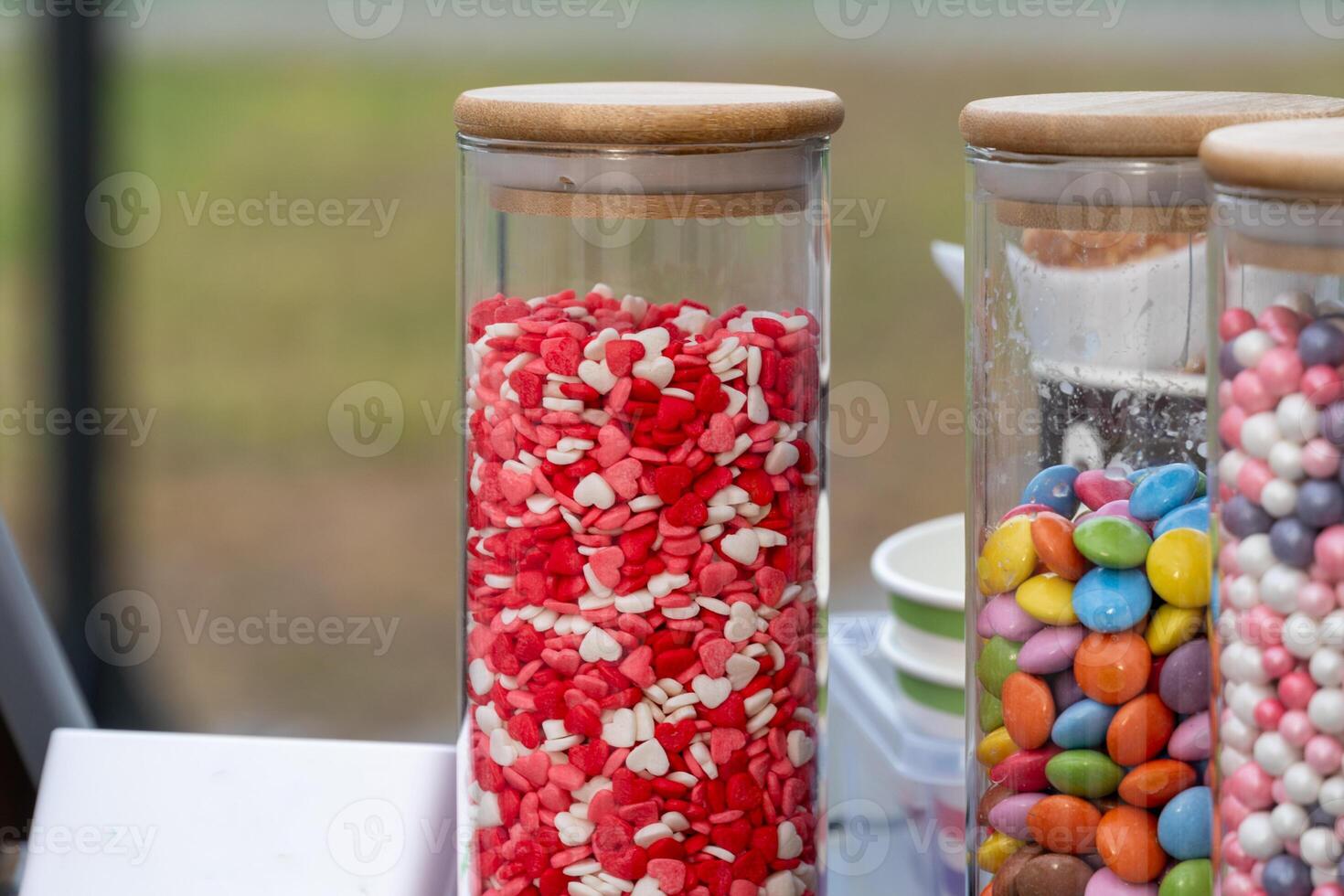 Clear jars filled with vibrant heart-shaped candies and colorful chocolate-coated sweets attract attention at an outdoor celebration in the afternoon light photo