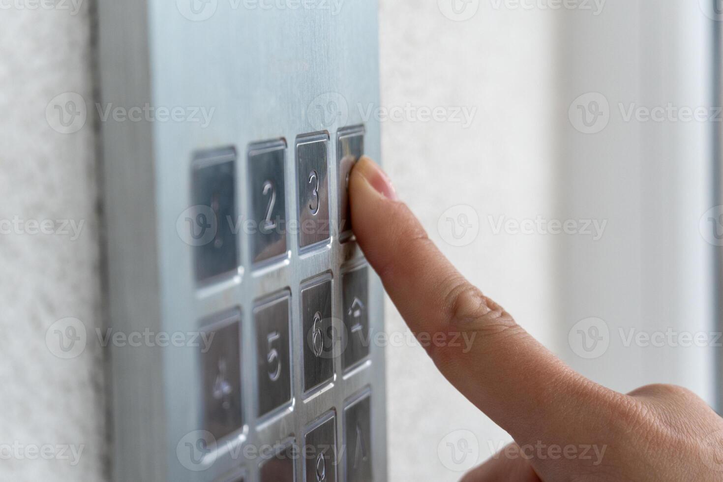 A person is using their finger to press the number three on a metallic keypad located beside a door. Bright light fills the area, indicating daytime photo