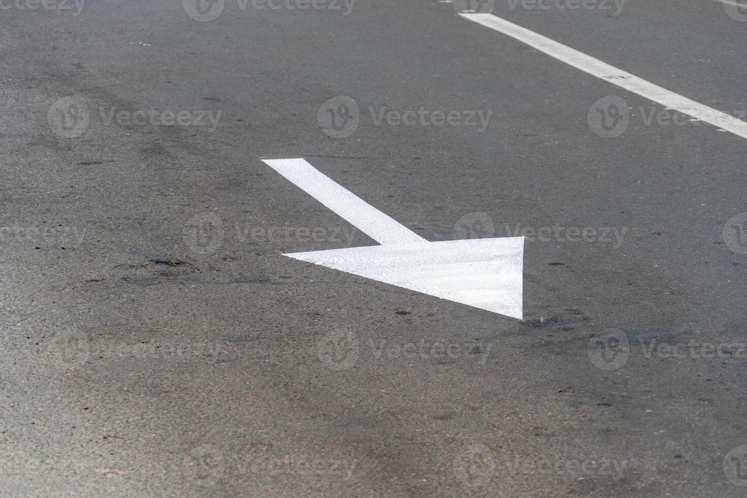 A clear white arrow is marked on the asphalt surface, guiding vehicles to turn left at a busy urban intersection under bright daylight photo