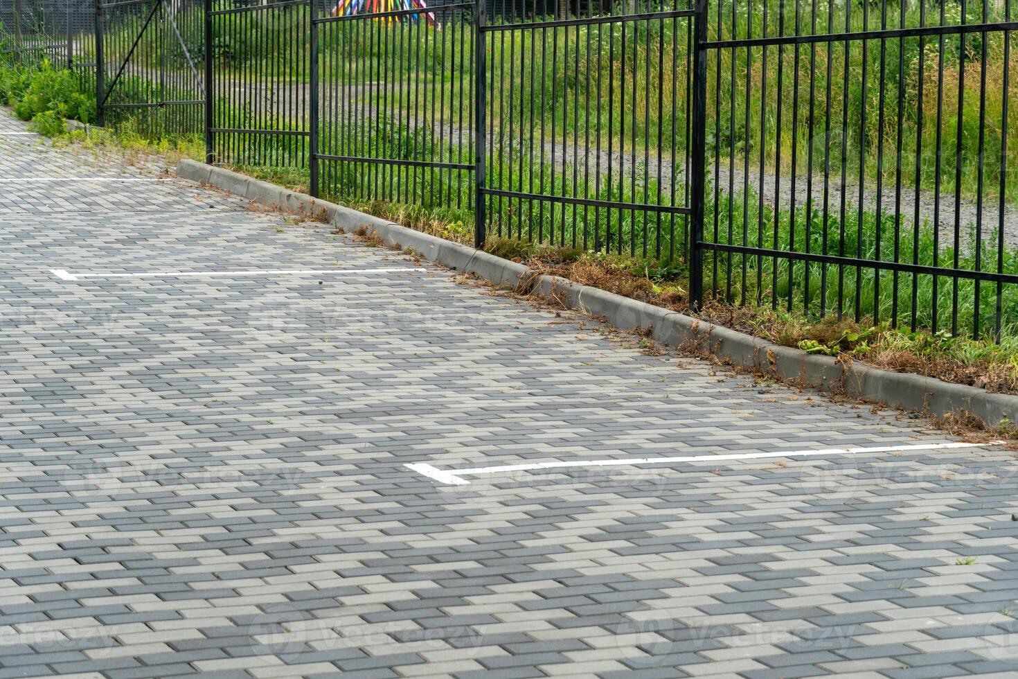 A neatly paved parking area features clearly marked spaces, bordered by a black metal fence and green grass. The setting appears tranquil and well-maintained photo