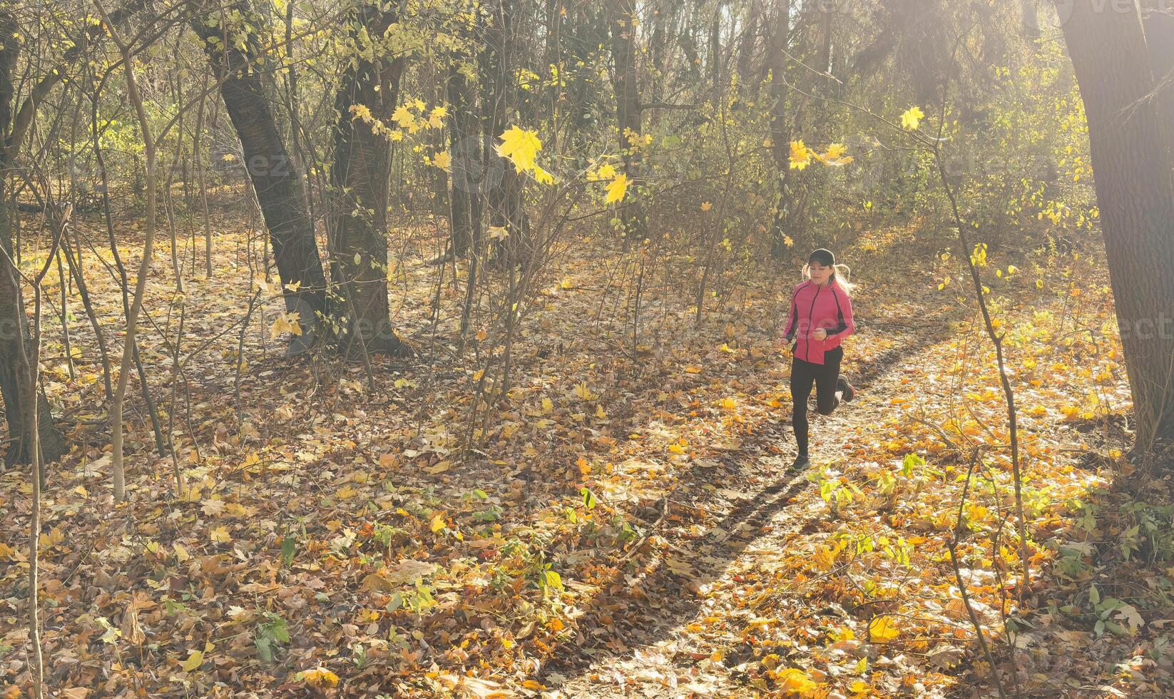 Woman running in autumn fall forest. Female runner training outdoor in profile. Healthy lifestyle image of young woman jogging outside. Fit ethnic Asian Caucasian fitness model. photo