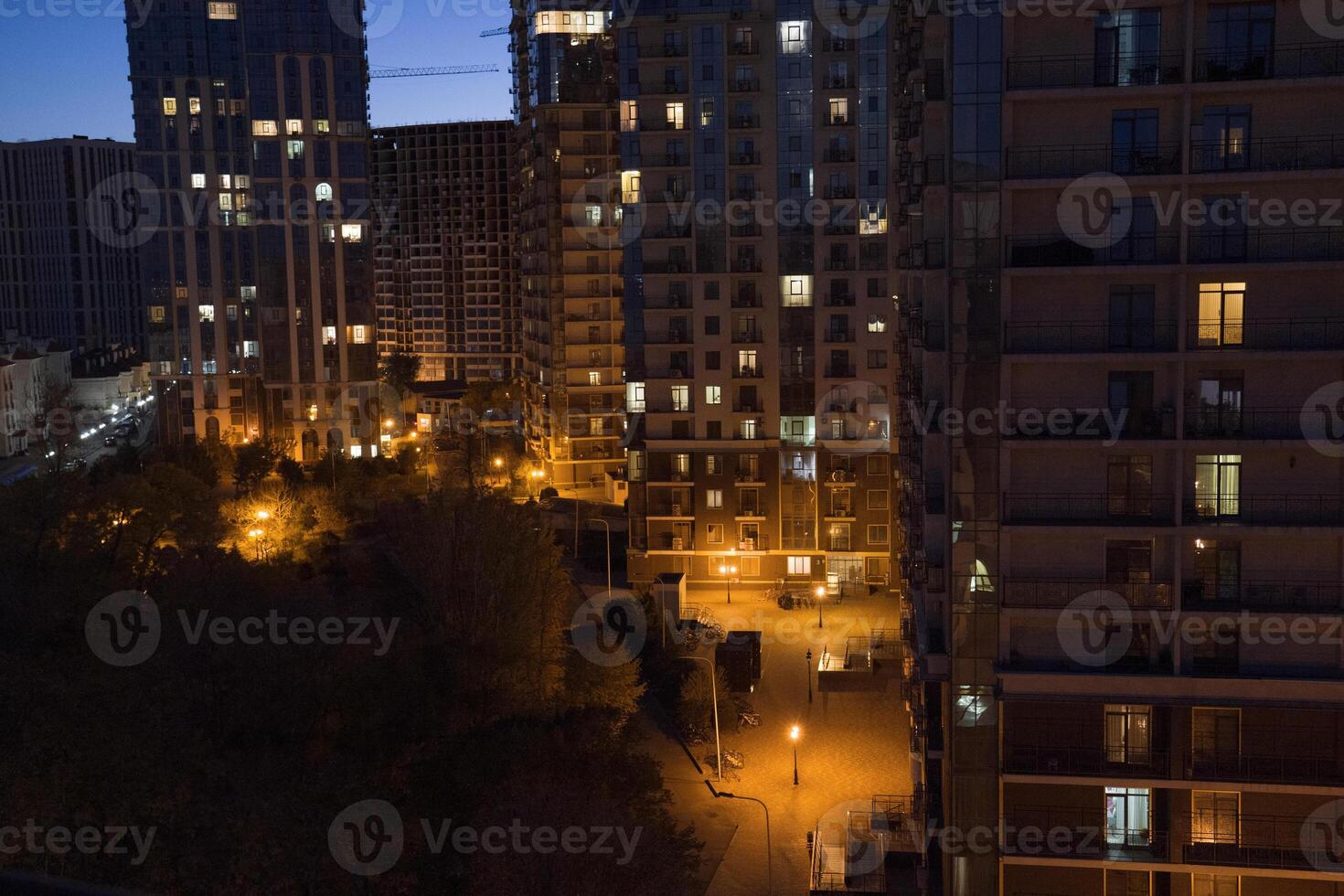 Urban night scene showcasing illuminated buildings and a park, with streetlights casting a warm glow on pathways, creating a serene atmosphere in a bustling city environment photo