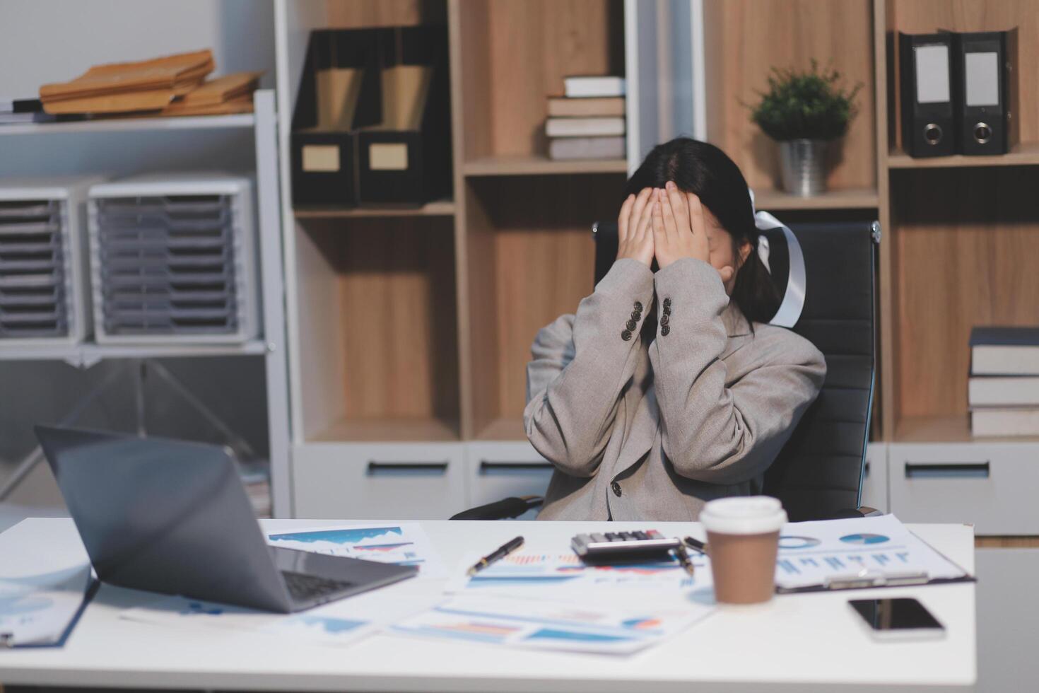 A woman in a business suit sitting at a desk with her hands on her head photo