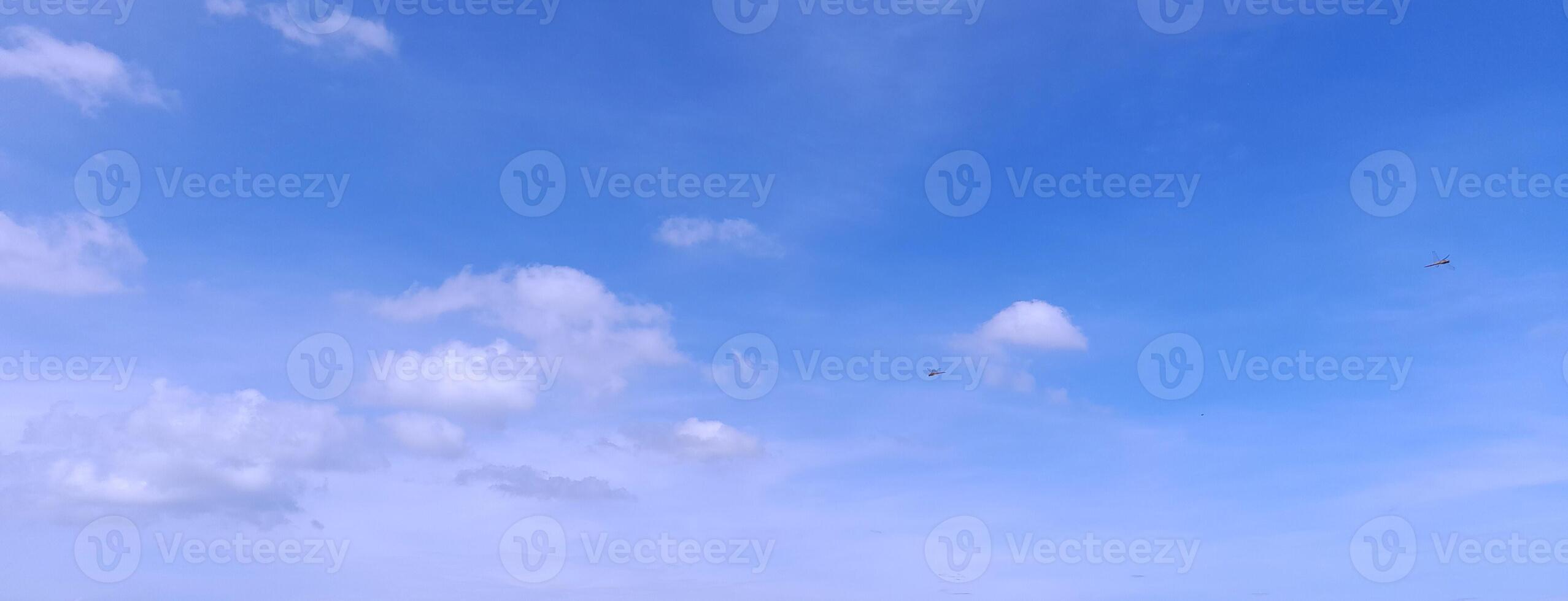 A clear blue sky with a few scattered white clouds and distant kites flying, creating a peaceful and open atmosphere. photo