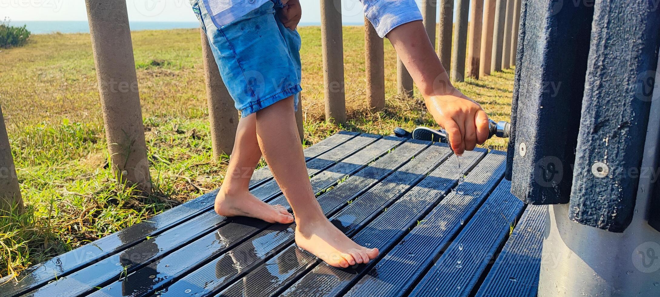 Boy, toddler a washes his feet from sand under the shower on the beach of Portugal close-up. Concept of summer, beach vacation with a child photo