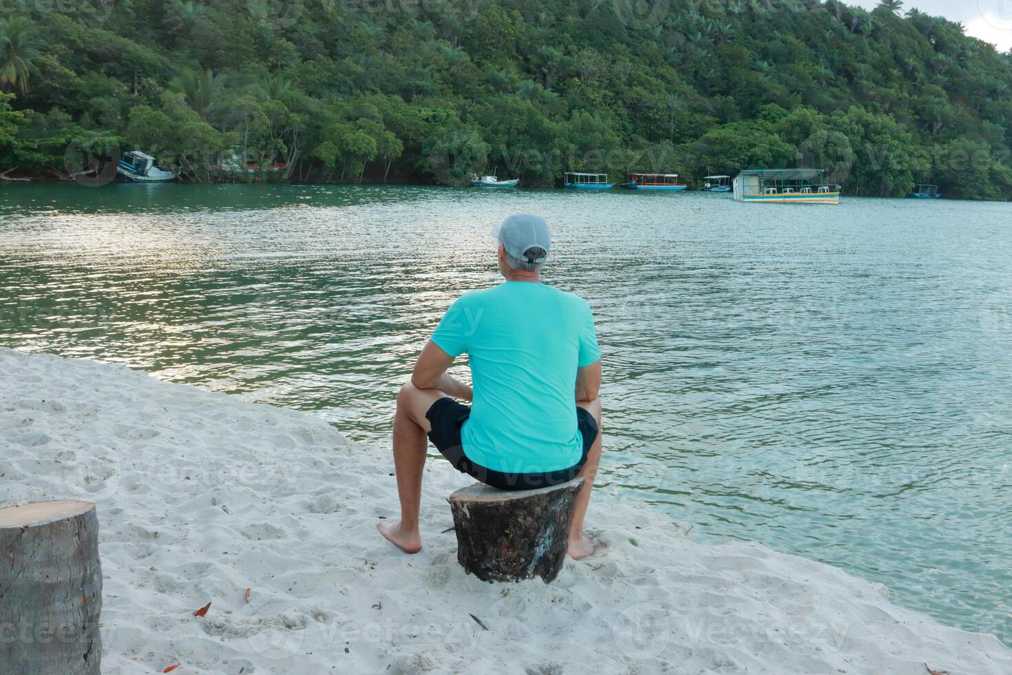 Man sitting on a stump looking out over the river photo