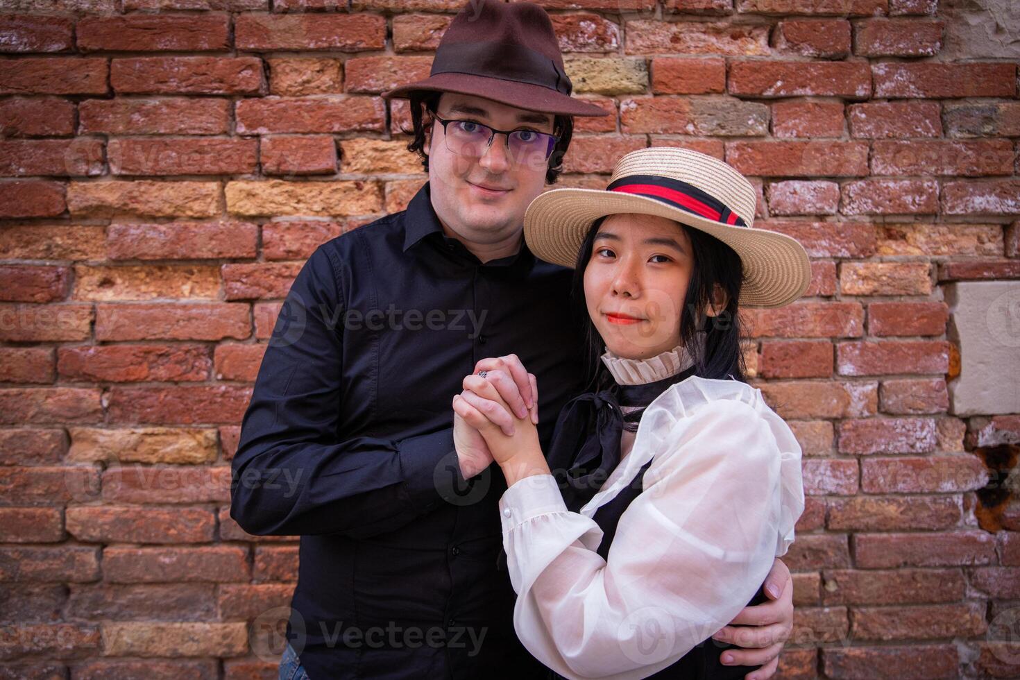 Young couple standing near red tile wall embraces with fingers crossed and looks to camera photo