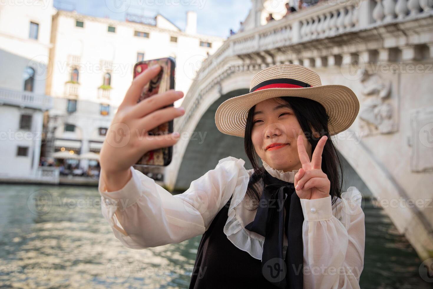 Smiling tourist does the V sign of victory under the Rialto bridge in Venice while taking a selfie photo