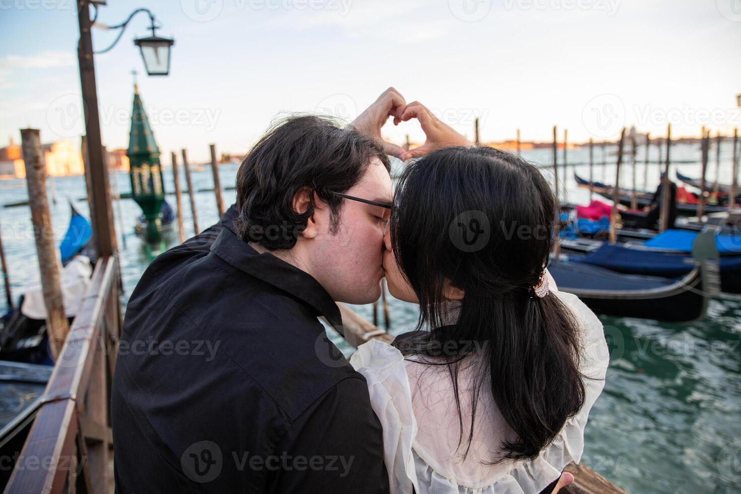 A couple of lovers kisses in Venice during the sunset and they make a heart with their hands, a romantic moment. photo