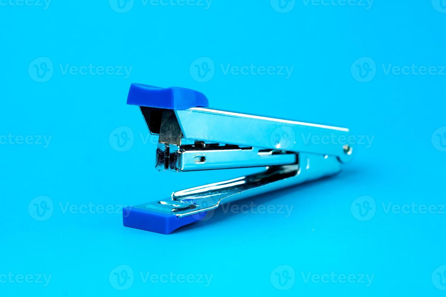 A silver metal stapler with blue plastic accents on a blue background. A compact and durable office tool designed for binding papers efficiently. Ideal for school, office, and home use. photo