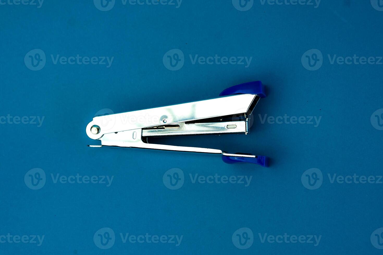 A silver stapler with blue plastic accents on a blue background. A compact and durable office tool designed for binding papers efficiently. Ideal for school, office, and home use. photo