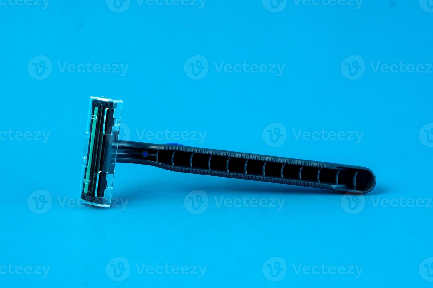 A blue disposable razor with a protective cap placed on a bright blue background. The ergonomic handle and sharp blade make it ideal for shaving facial or body hair safely and smoothly photo