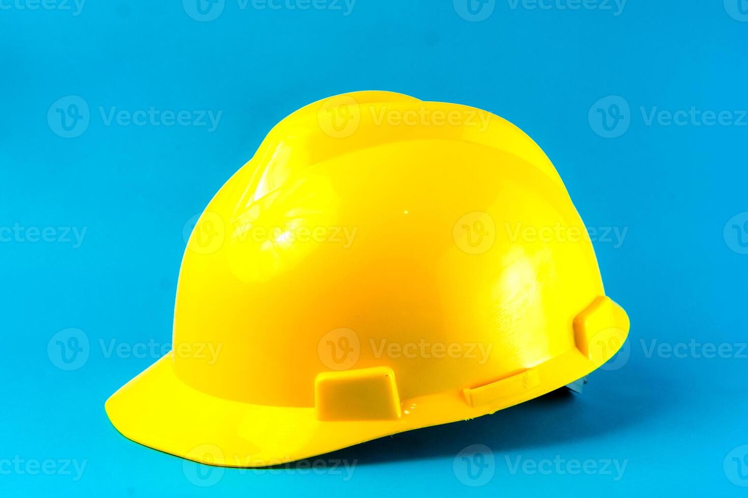 A bright yellow construction hard hat on a blue background. Safety helmet for industrial workers, engineers, and builders, symbolizing workplace protection and occupational safety. photo