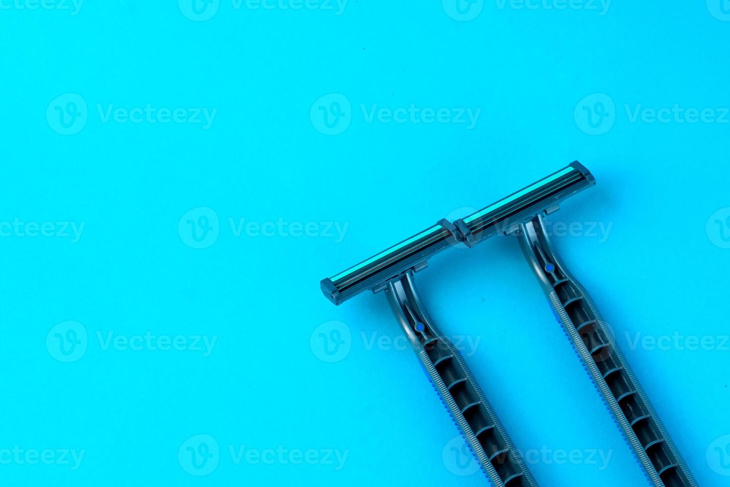 Two disposable razors with black handles on a bright blue background. Minimalist grooming tools for a smooth shave, personal care, and hygiene routine. photo