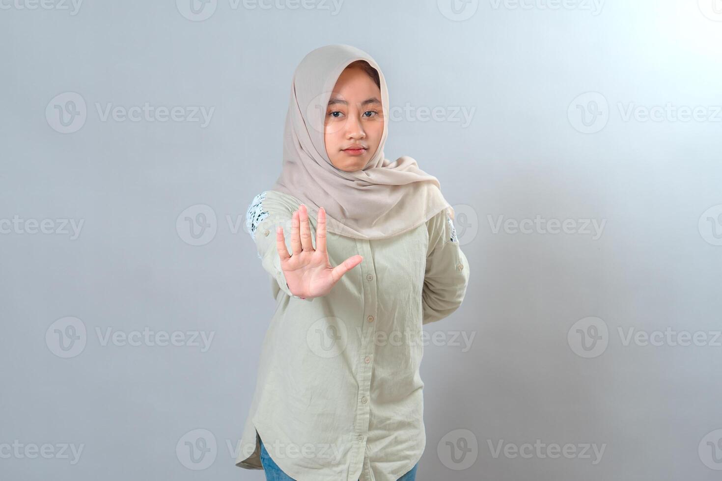 Serious young Muslim woman wearing hijab raising her hand in stop gesture while looking directly at the camera. Her firm facial expression shows assertiveness and clear boundaries. photo
