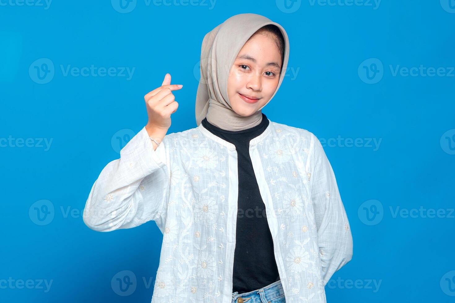 A Happy young Asian woman wearing hijab smiling warmly while showing finger heart gesture. Friendly and positive facial expression, perfect for advertising and marketing use photo