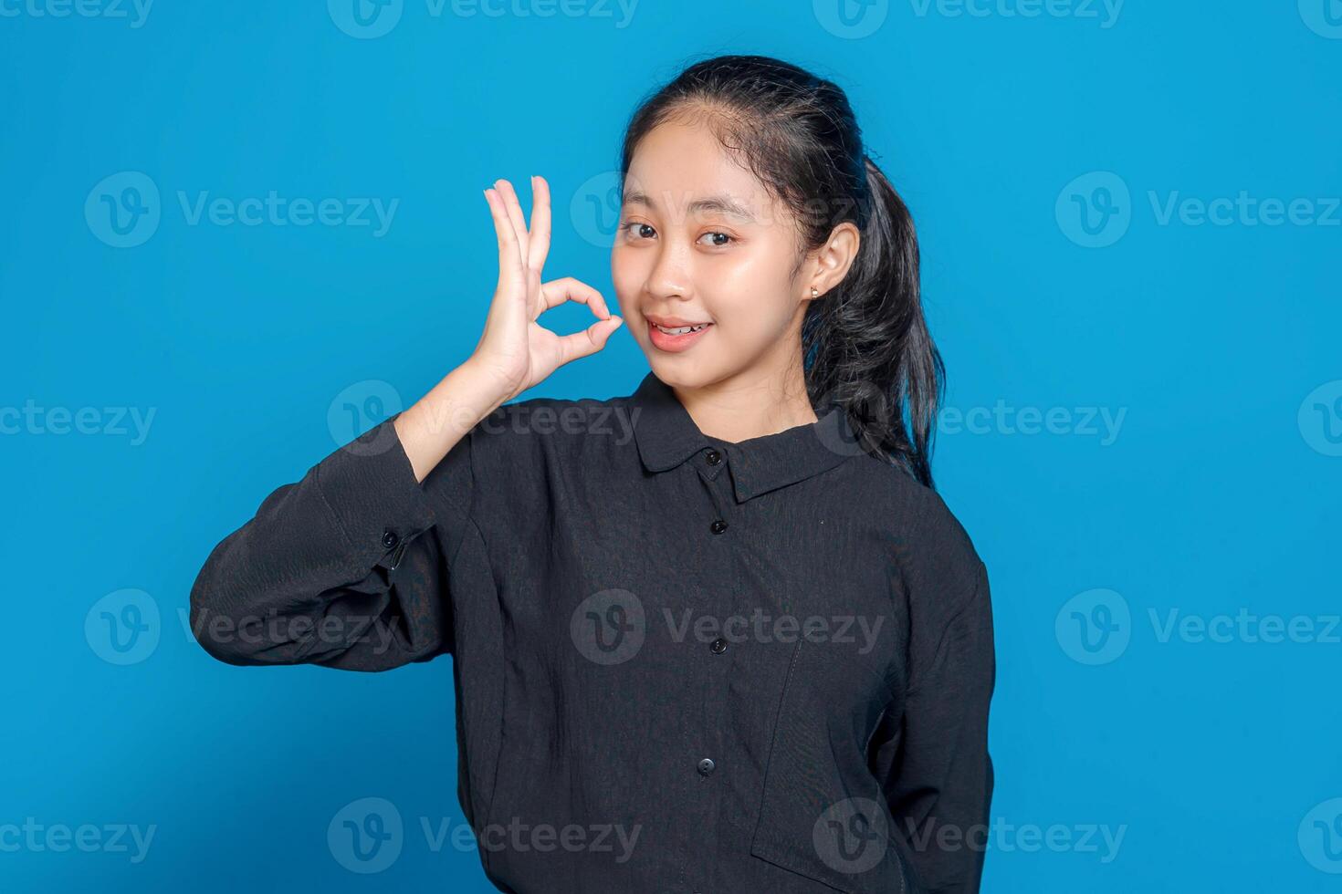 Smiling young Asian girl making an OK hand gesture with a confident and friendly facial expression. Perfect image for positive, modern advertising concepts. photo