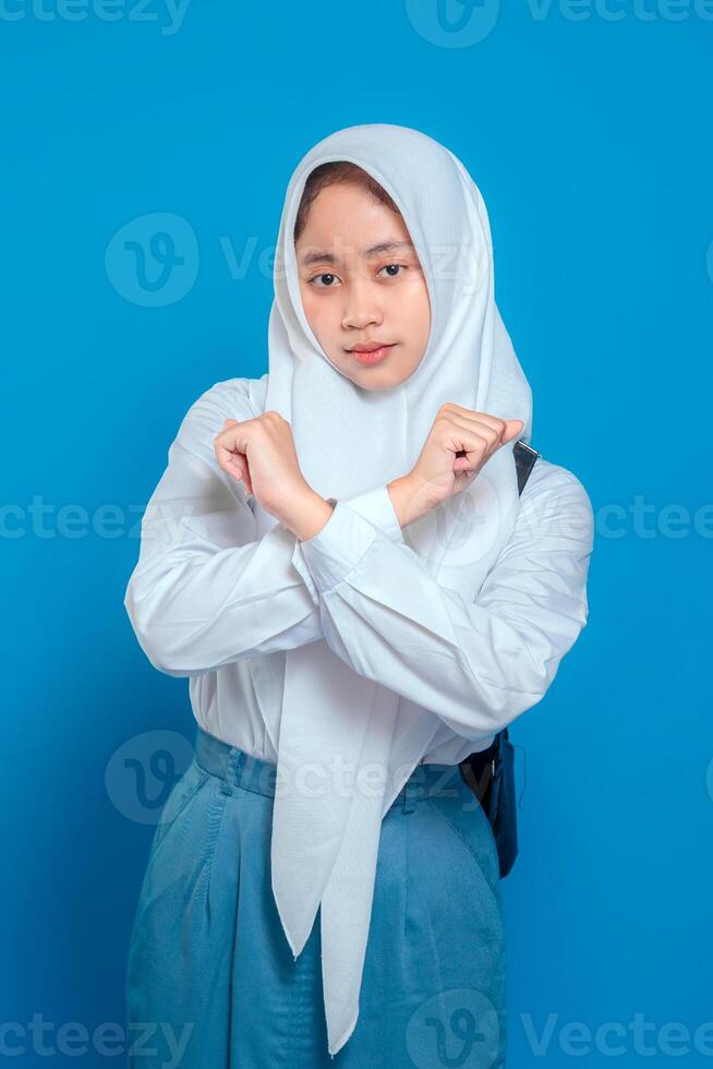 Muslim student wearing school uniform and hijab making crossed arms gesture with serious facial expression. Back to school concept with educational and disciplinary theme. photo