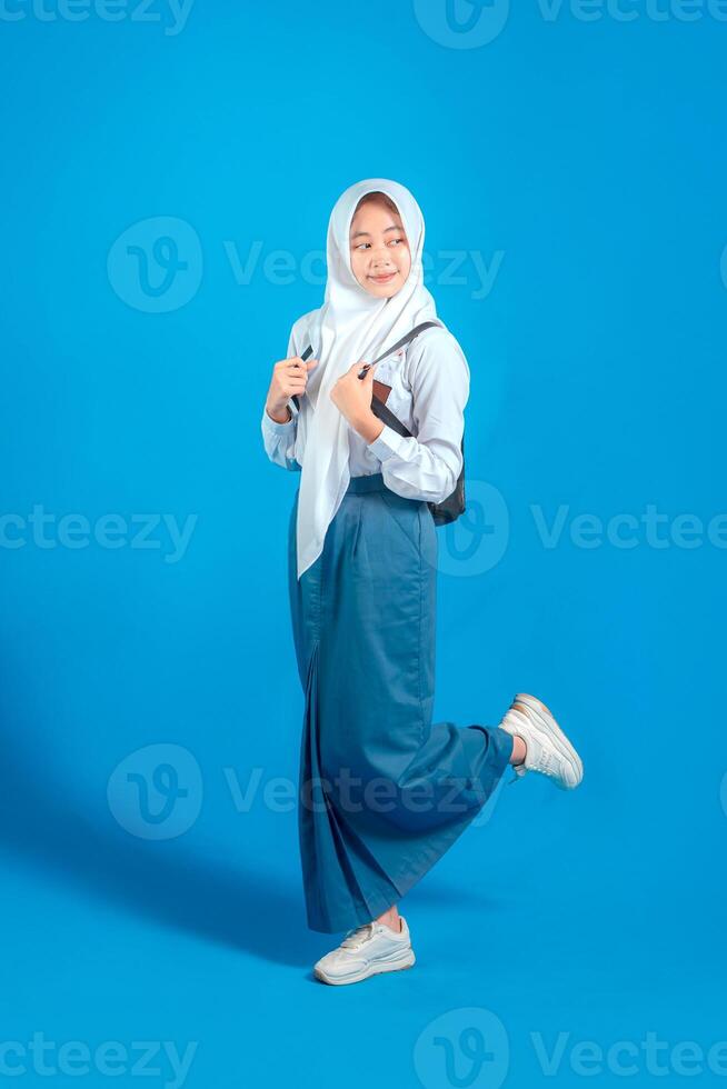 Asian Muslim teenage girl student smiling confidently while carrying backpack and holding pencil, ready to study and learn, education and back to school concept. photo