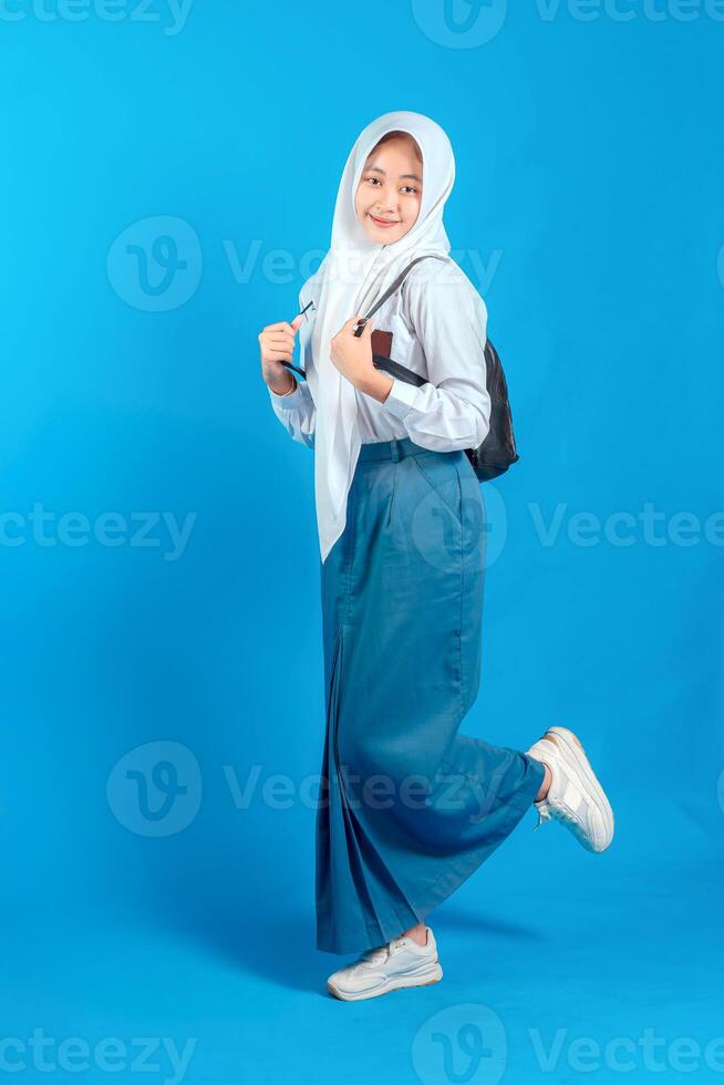 A Asian Muslim teenage girl student smiling confidently while carrying backpack and holding pencil, ready to study and learn, education and back to school concept. photo