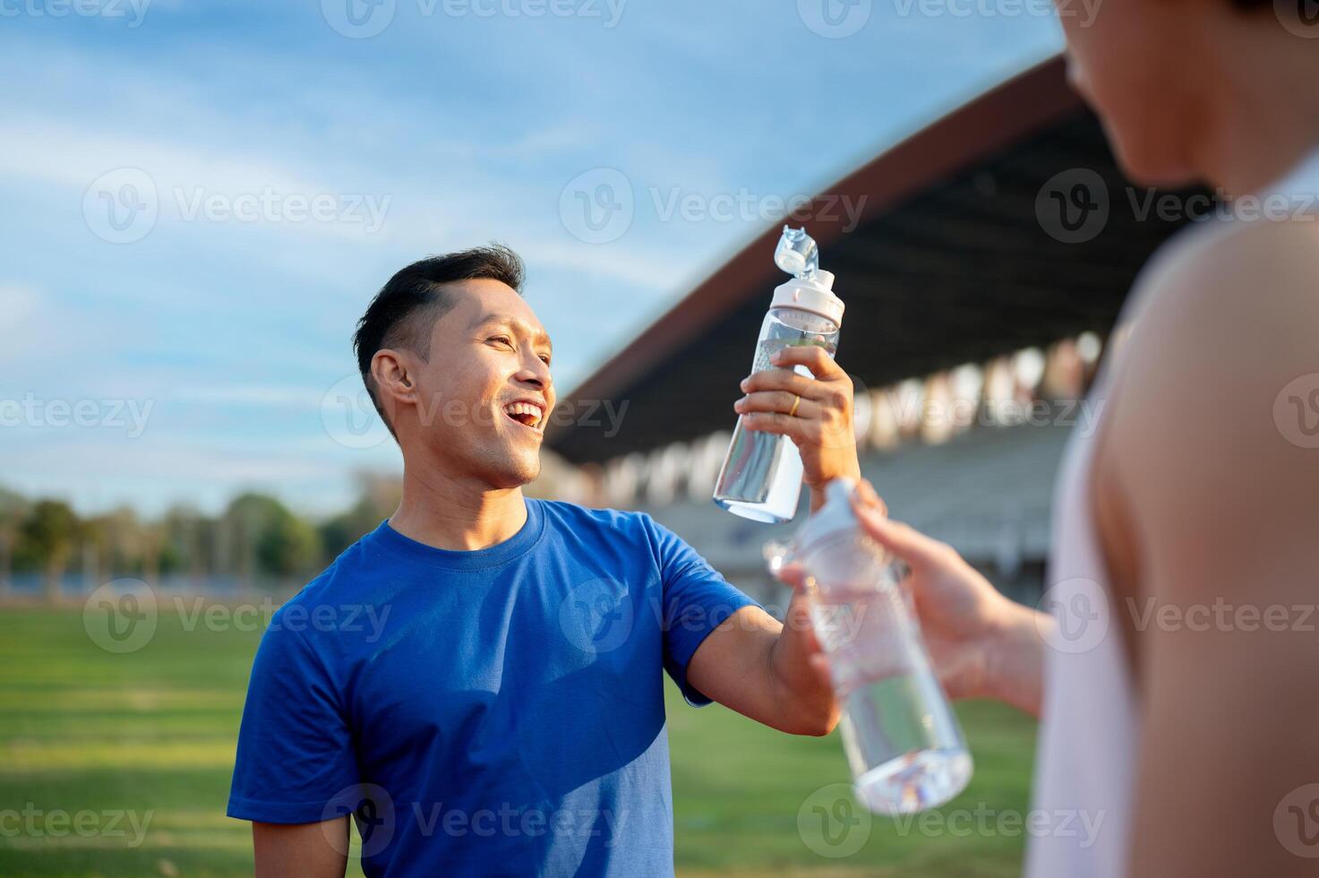 Two asian athlete men holding and looking at their water bottles while talking together on racetrack photo