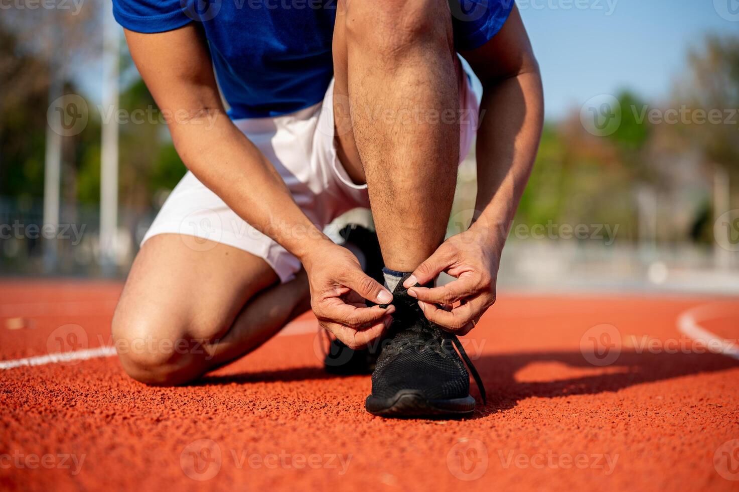 Close up of a man crouching while tying his black sneaker shoelace on racetrack. Outdoor exercise. photo