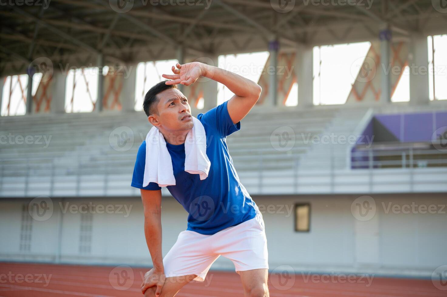 Asian man in blue t shirt is standing with hands on his knee and looking up with hand over eyes. photo