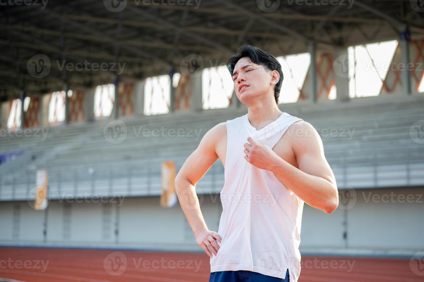 Asian man standing with one hand on waist and other hand grabbing a white tank top. Hot or tired. photo