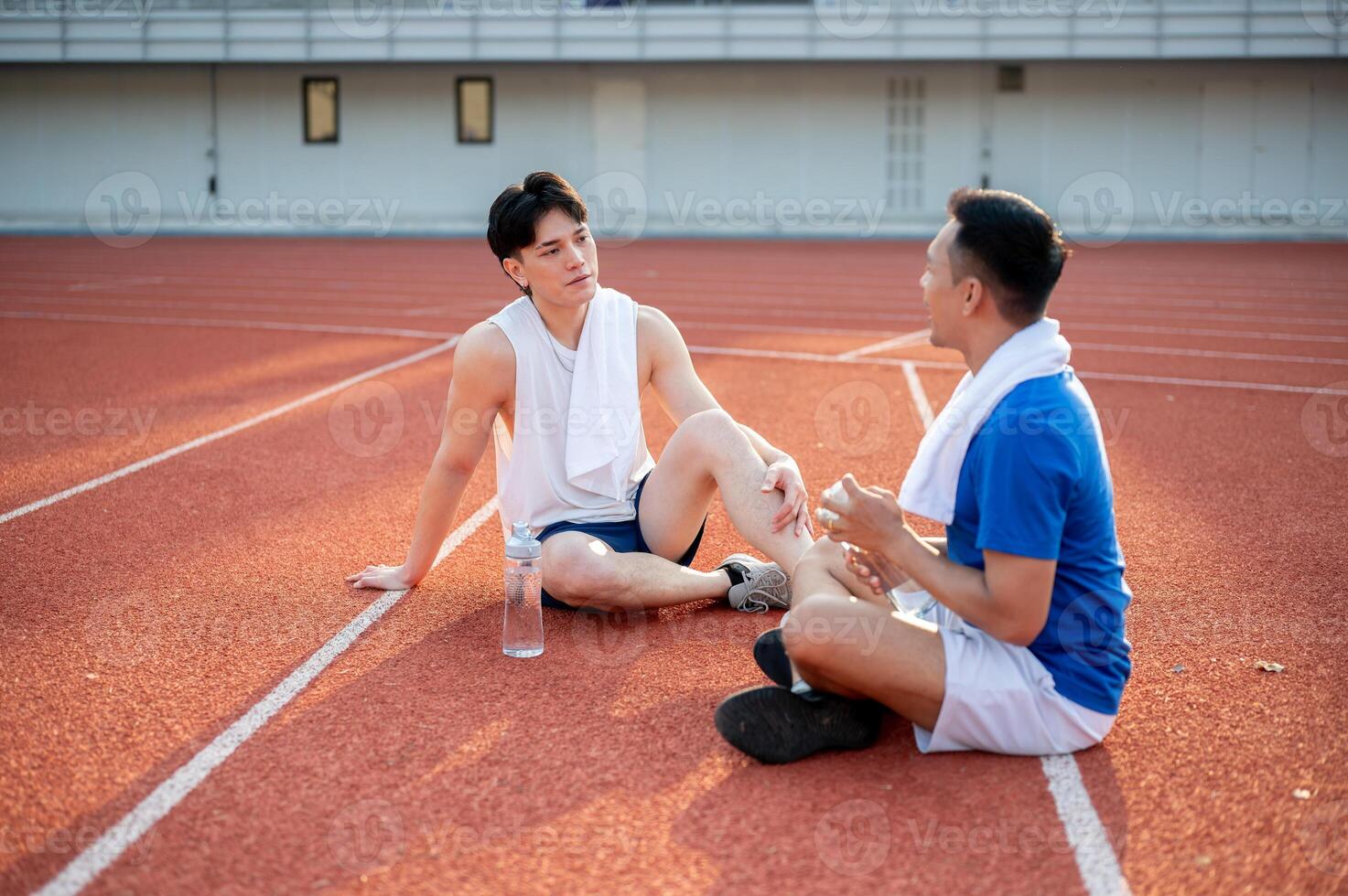 Two asian athlete men are taking a rest, sitting together on the racetrack. Jogging or Running. photo