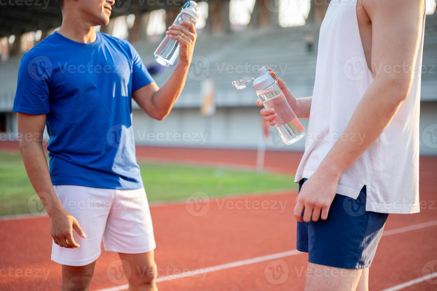 Two asian athlete men are holding their water bottles while talking together on the racetrack. photo